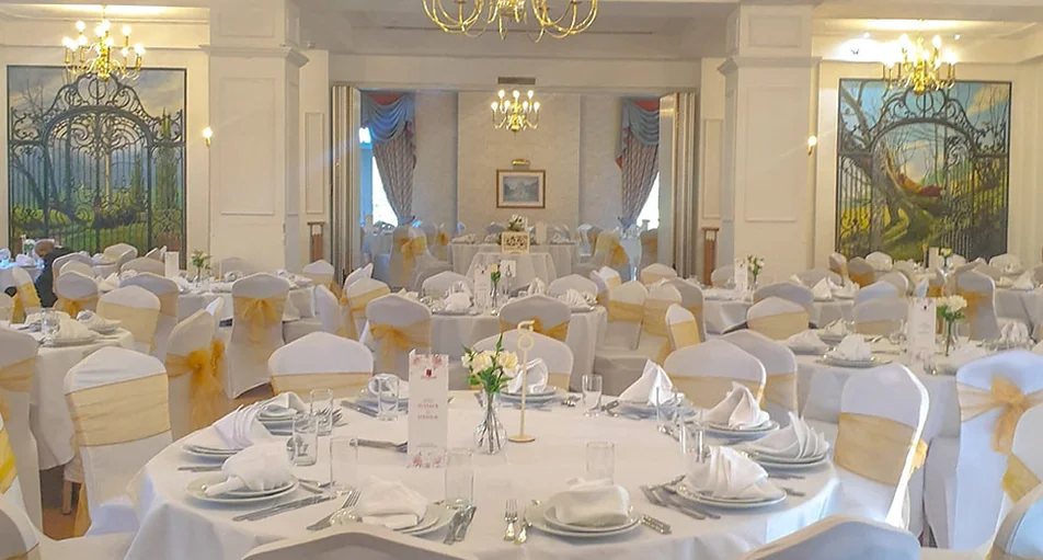 Elegant banquet hall with gold chairs, white round tables and stained glass windows