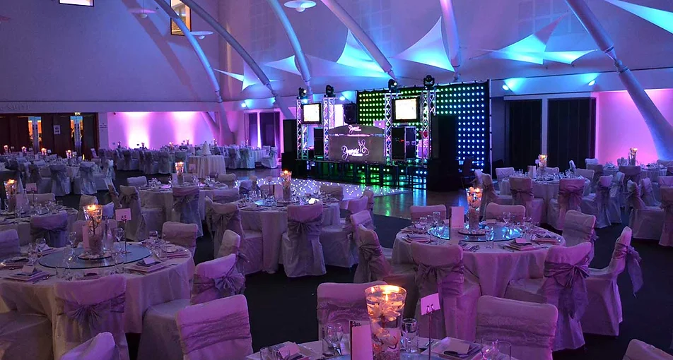 Banquet hall reception with purple mood lighting, DJ booth and round tables