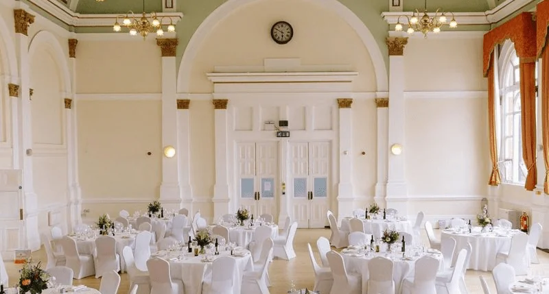 Grand hall wedding venue with round tables set beneath ornate archways and chandeliers