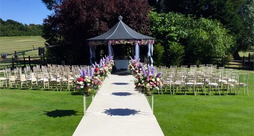 Outdoor wedding ceremony gazebo with aisle lined by white chairs