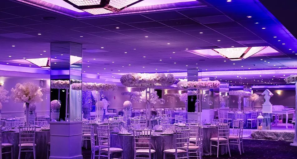 Wedding venue reception hall lit in blue and purple with tables set for guests