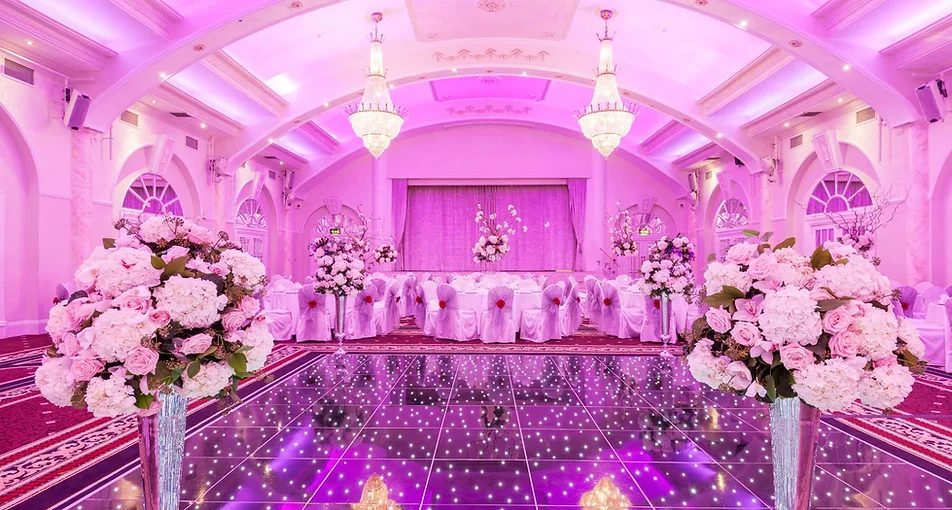 Wedding reception hall interior decorated with pink lighting and floral table settings