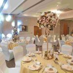 Banquet hall table set with gold linens and a tall pink and white flower centrepiece