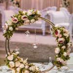 Round floral wreath centrepiece with hanging crystals on a table, elegant lounge seating in background
