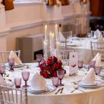 Round banquet table set with candles, a red rose centrepiece and purple glassware
