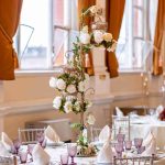 Wedding banquet hall with round tables set in white and gold, orange drapery and floral decor