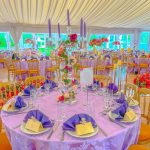 Colourful wedding table setting with purple and yellow napkin styling in a marquee