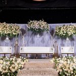 Wedding stage backdrop with cream floral arrangements on gold frames, white sofa seating, and a starlit canopy