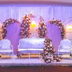 White wedding stage sofa flanked by tall candle stands and floral arrangements