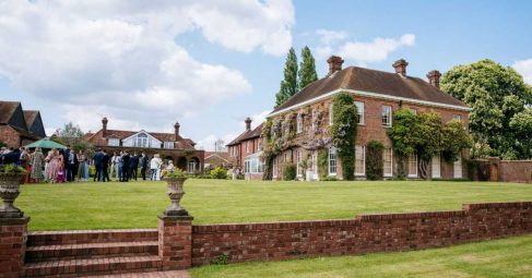 Red brick manor house venue with guests gathering on the lawn