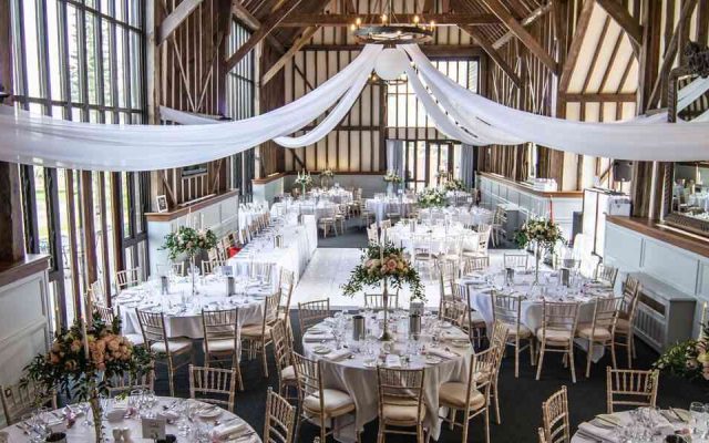 Timber-framed barn wedding venue set with round tables and white drapery
